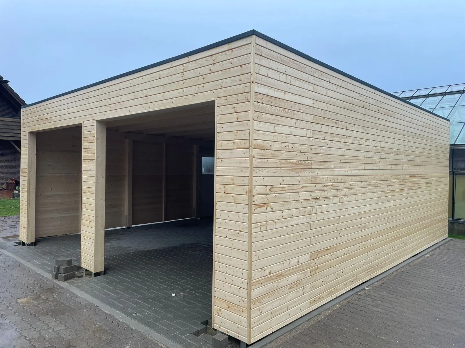 Rohbau einer Doppelgarage aus hellem Holz auf einer Baustelle, Wände und Flachdach bereits montiert