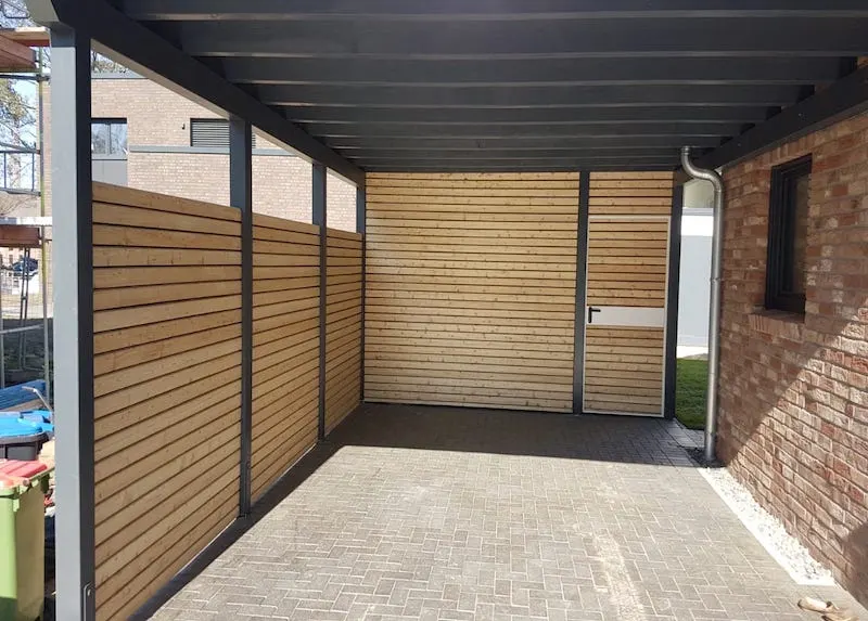 Carport-Innenansicht mit Wänden aus Lärchenholz, anthrazitfarbenen Trägern und Tür zum Abstellraum