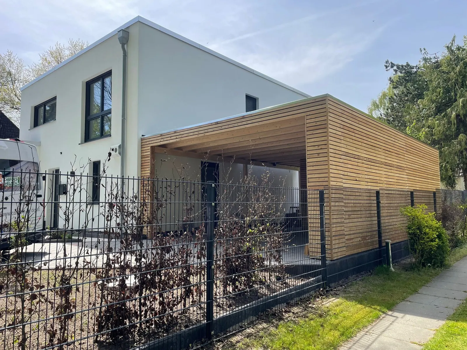 Kubischer Carport mit horizontaler Lärchenfassade und dunklem Flachdach neben einem modernen weißen Wohnhaus