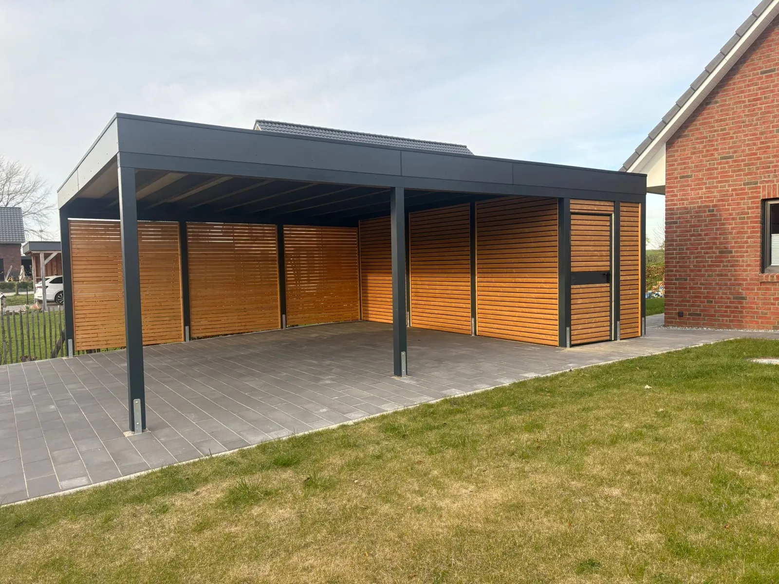 Doppelcarport mit anthrazitfarbenem Flachdach und hellen Holzwänden an einem roten Klinkerhaus