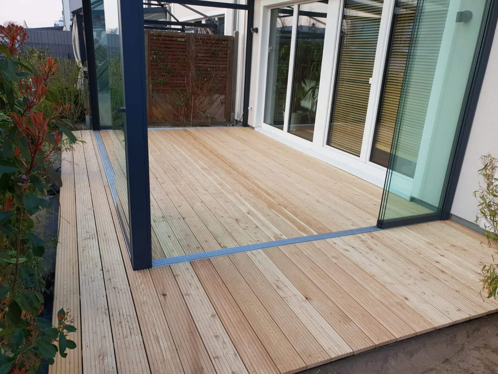 Rahmenlose Glasschiebewände mit flächenbündiger Bodenschiene zwischen Lärche-Terrassendielen